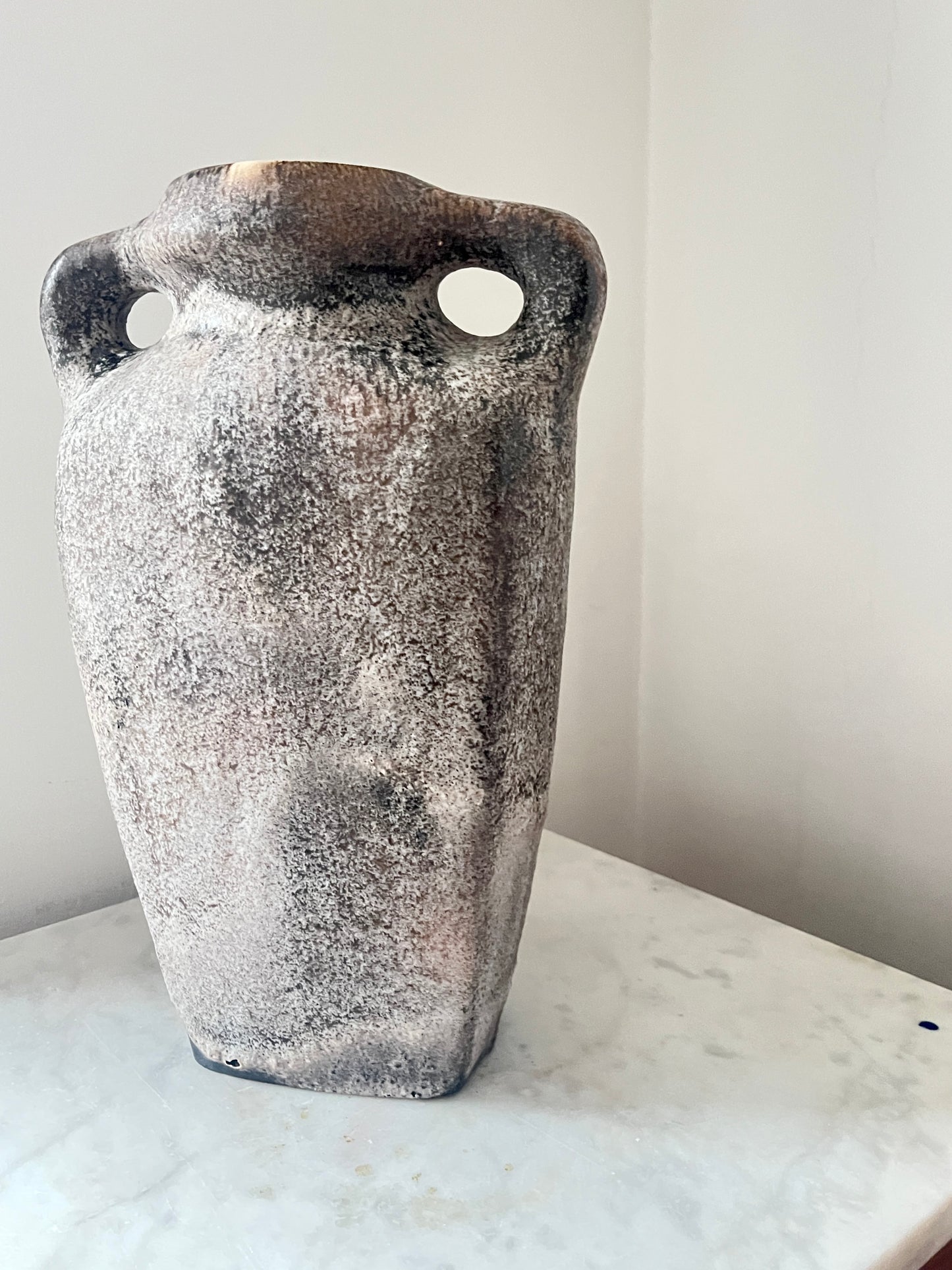 Textured vase with handles on a marble surface against a white wall